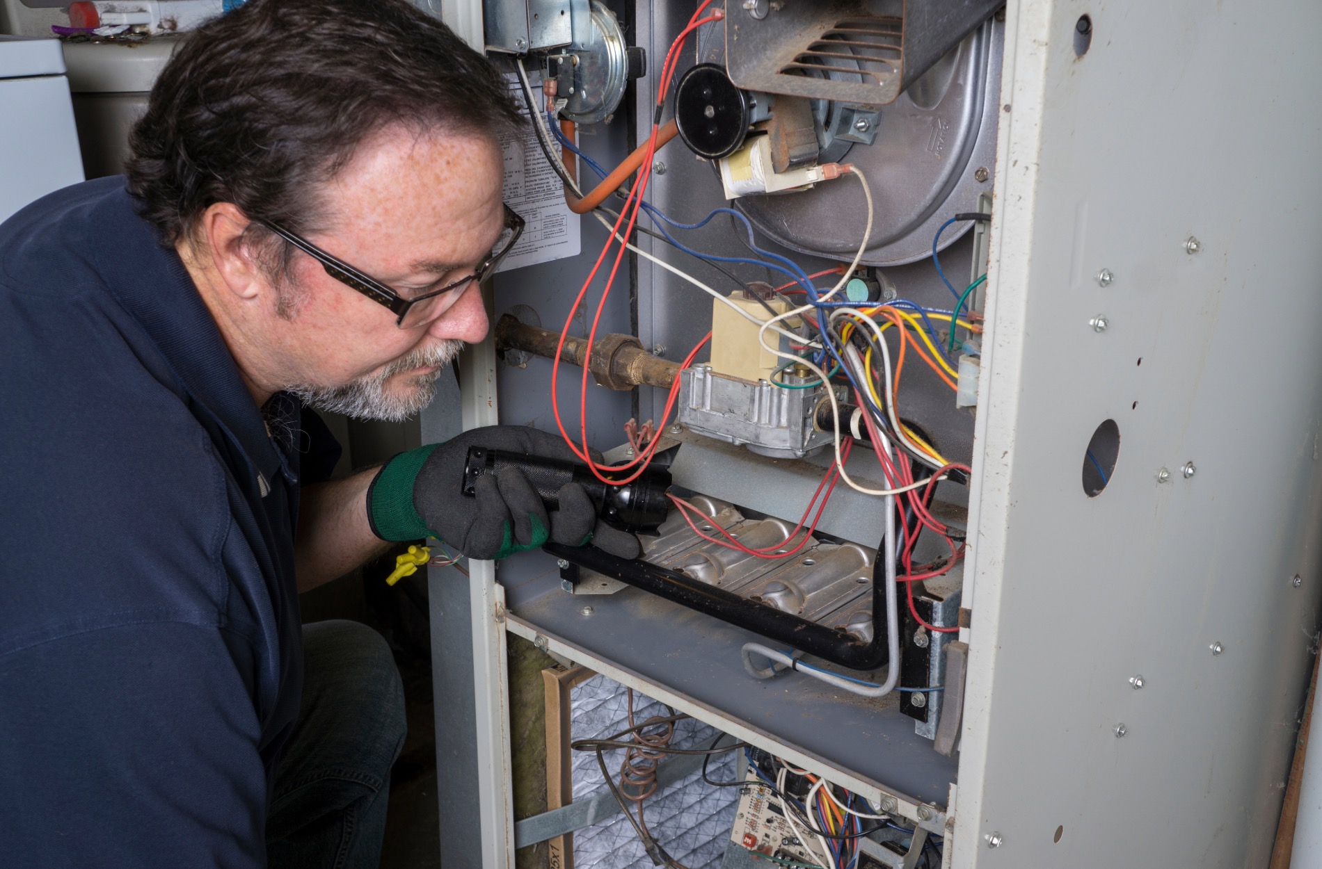 A technician is repairing an furnace, focused on the unit with tools in hand, in a well-lit environment.